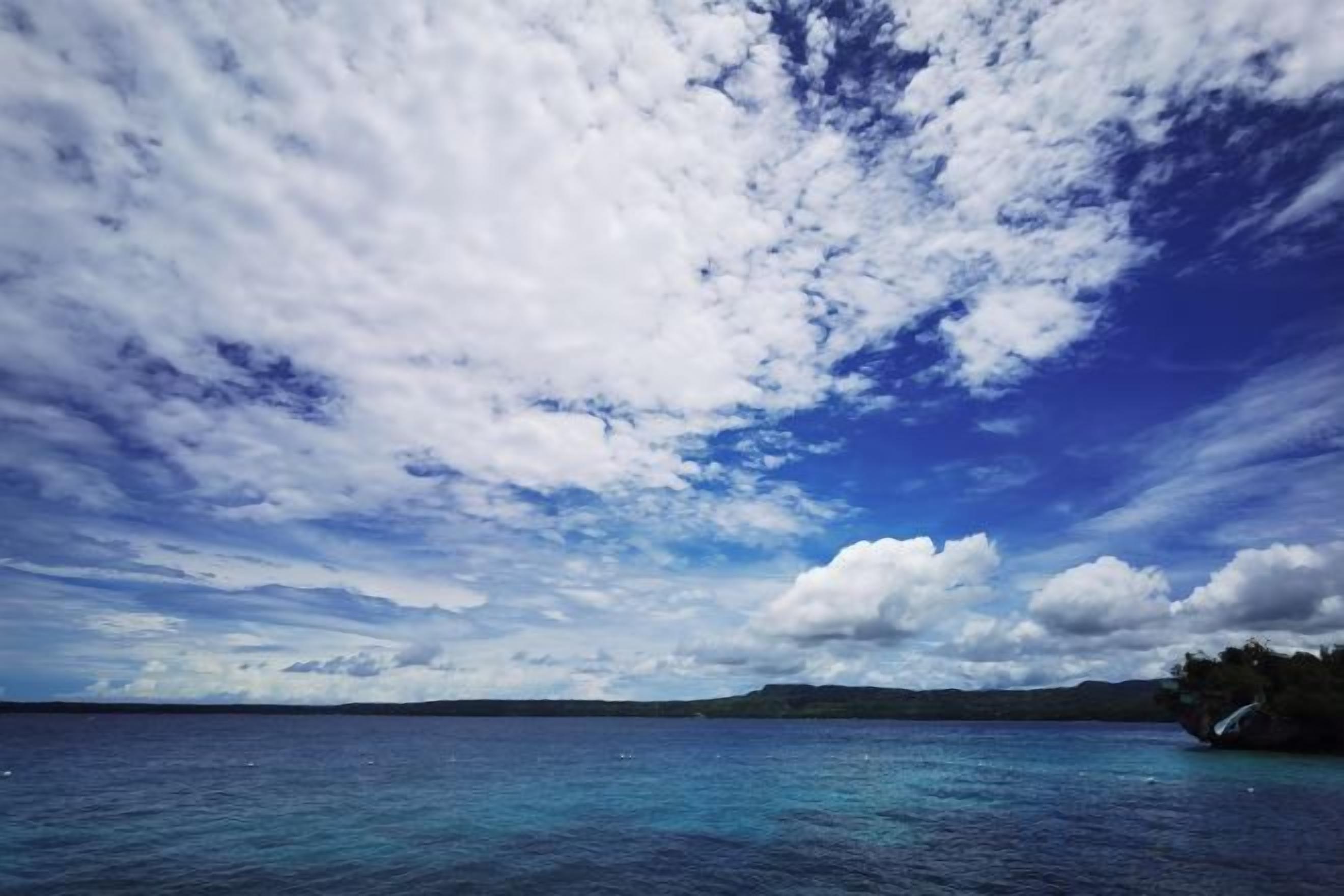 Vista de un cuerpo de agua con una masa de tierra distante y un cielo parcialmente nublado.