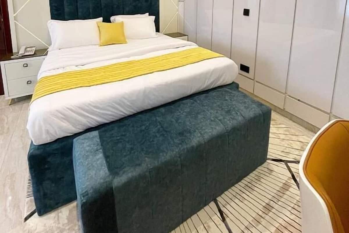 A modern bedroom with a large bed, a bedside table, a wardrobe, and a bench.