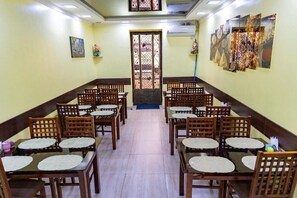 Un espace repas avec des tables et des chaises en bois, une porte décorative centrale et des œuvres d’art mural.
