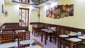 A restaurant with wooden tables and chairs, a staircase, and wall art depicting food. - Shakh Sultan Hotel (Tashkent)