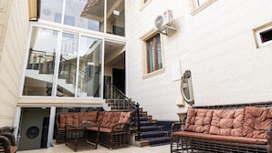 A multi-story building with a staircase leading to an upper floor. There are two brown cushioned sofas and a small table in the foreground. - Shakh Sultan Hotel (Tashkent)