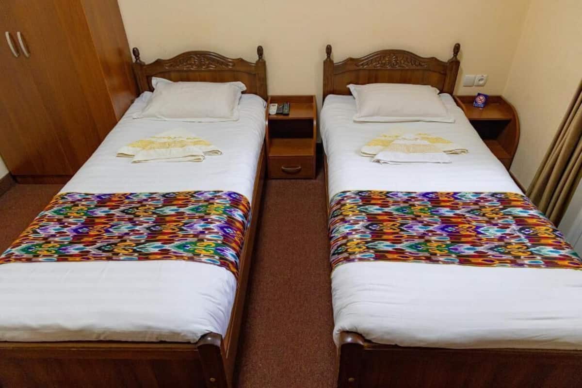 Two single beds with wooden headboards, a wooden wardrobe, and a small bedside table with a remote control and a tissue box.
