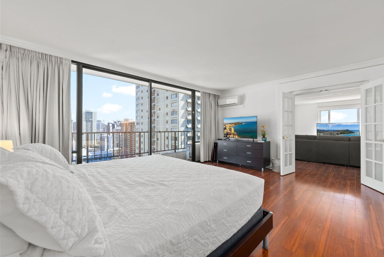 A modern hotel room with a large bed, a TV, a balcony with a city view, and a dining area.