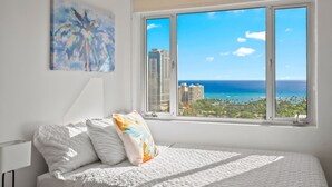 Un dormitorio con un ventanal que ofrece vistas al océano y edificios.