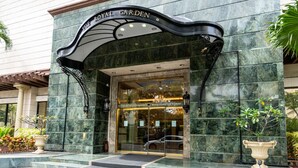 La entrada del Royal Garden Waikiki, con un imponente revestimiento de mármol, un gran dosel de acceso y un coche visible a través de las puertas de cristal.
