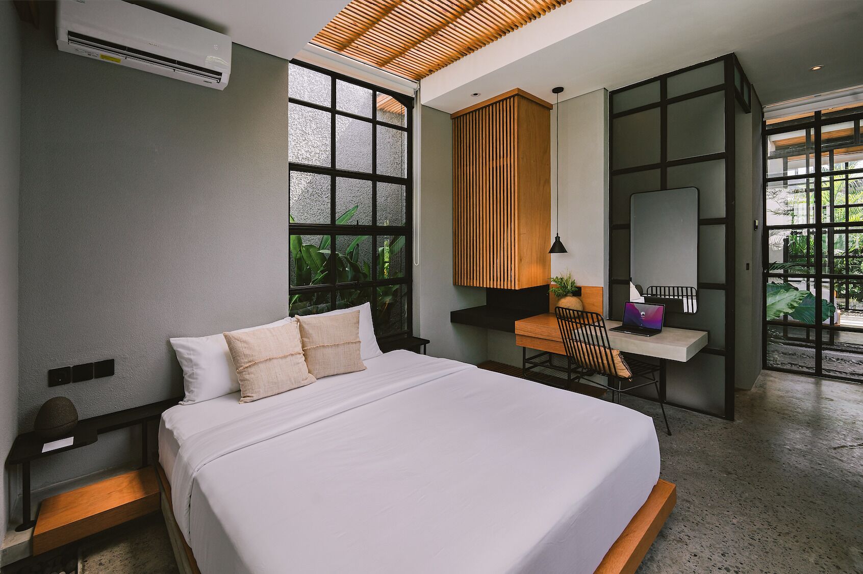 Une chambre moderne dotée d’un grand lit, d’un bureau et d’une chaise, avec une grande fenêtre offrant une vue sur la verdure environnante.