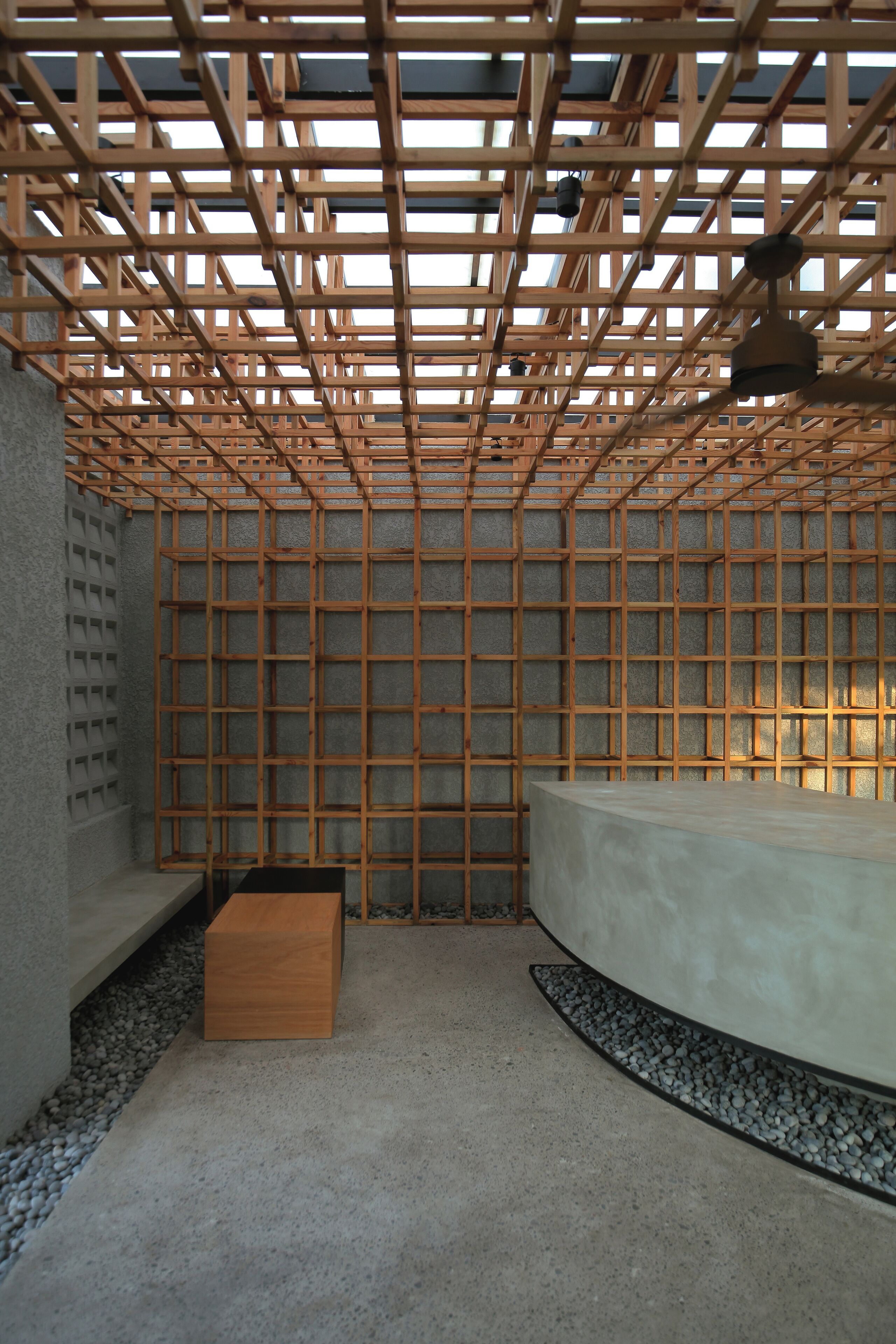 Una habitación con techo de celosía de madera, un banco de hormigón y una pared curva.