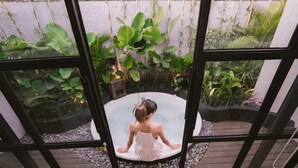 Eine Frau in einem weißen Kleid sitzt in einem Whirlpool, umgeben von üppiger Vegetation.