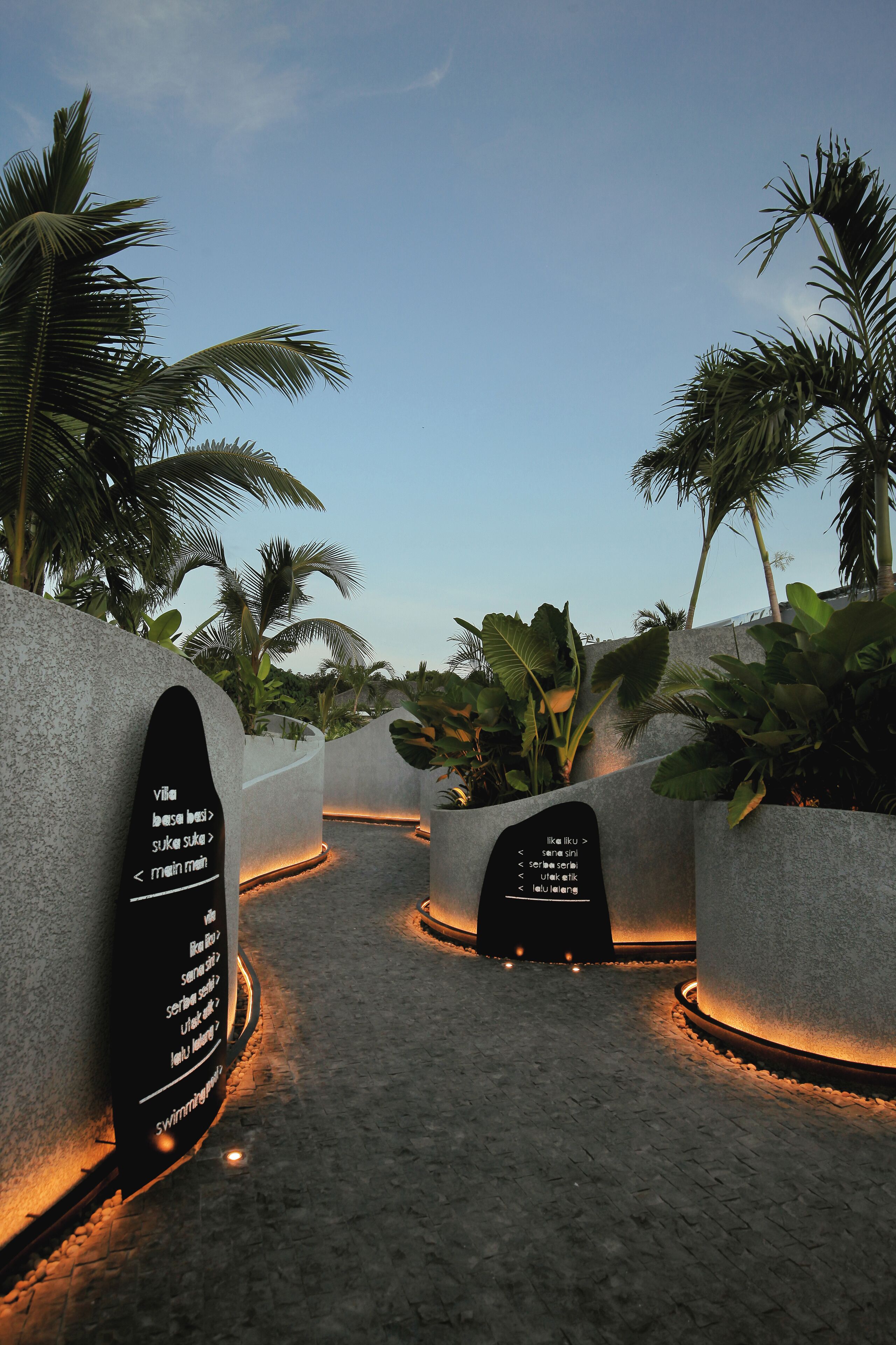 A pathway with illuminated signs and palm trees.