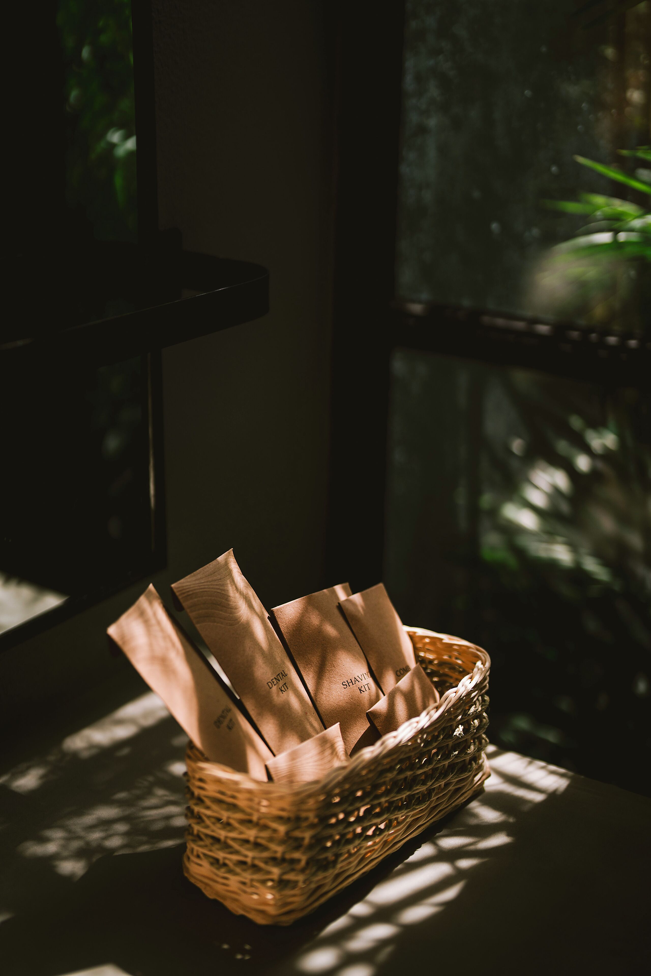 A wicker basket with brown paper bags on a table by a window.