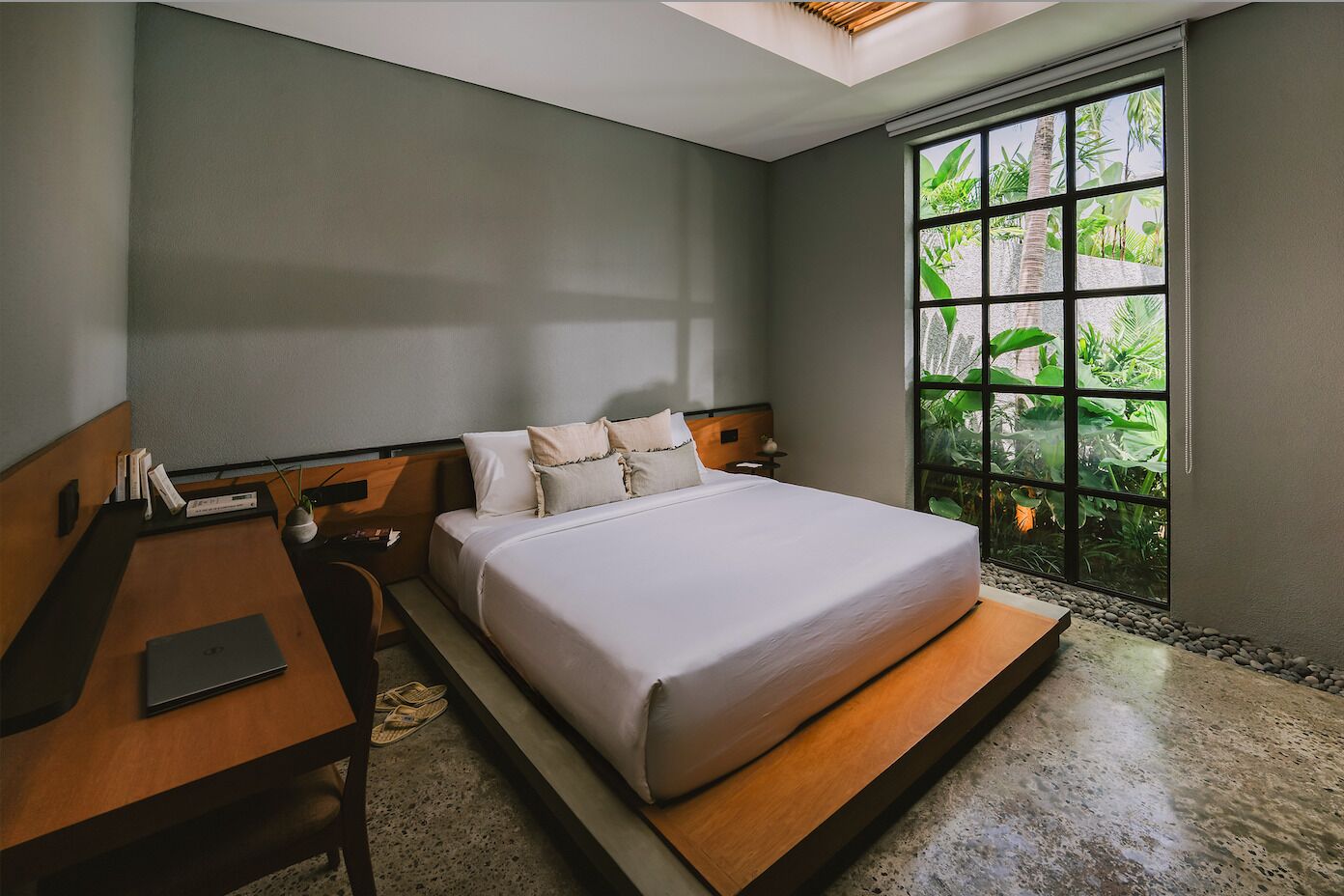 A modern hotel room with a large bed, a desk, and a view of greenery through a window.