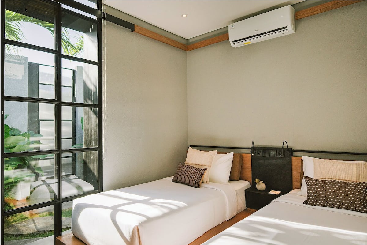 A bedroom with two beds, a window, and an air conditioning unit.