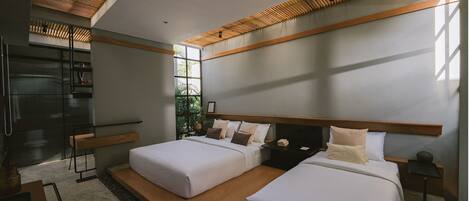 A modern bedroom with two beds, a built-in bench, a large window, and a kitchen area with a refrigerator.