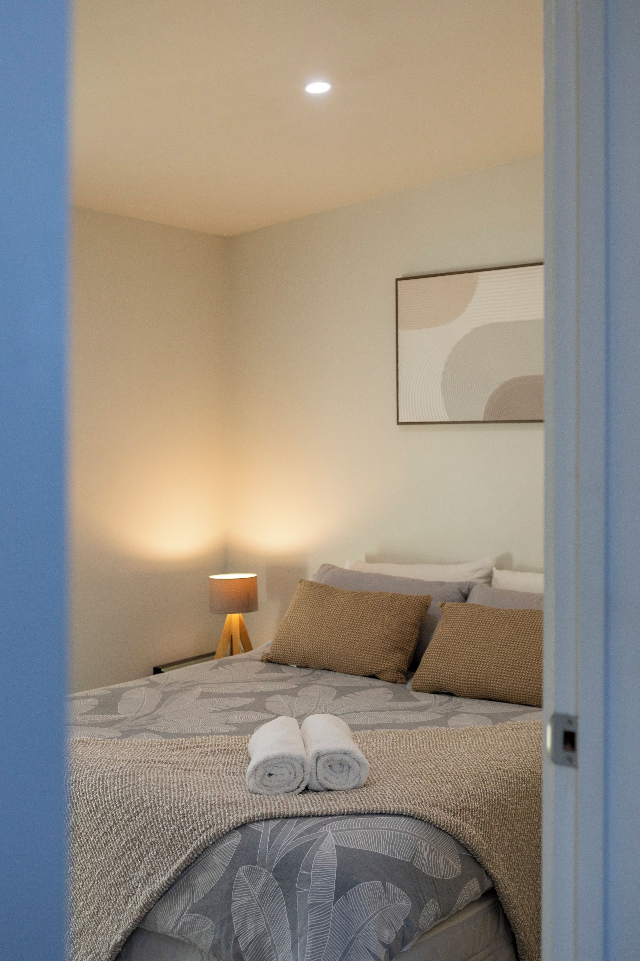 Un lit bien fait, avec une couvre-lit à motifs, une paire de serviettes enroulées et une lampe de chevet.