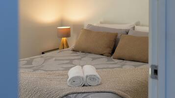 Un lit bien fait, avec une couvre-lit à motifs, une paire de serviettes enroulées et une lampe de chevet.