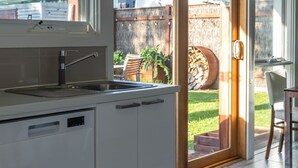 Een moderne keuken met een groot eiland, een inbouwvaatwasser en een schuifdeur naar een achtertuin met een barbecuehoek.