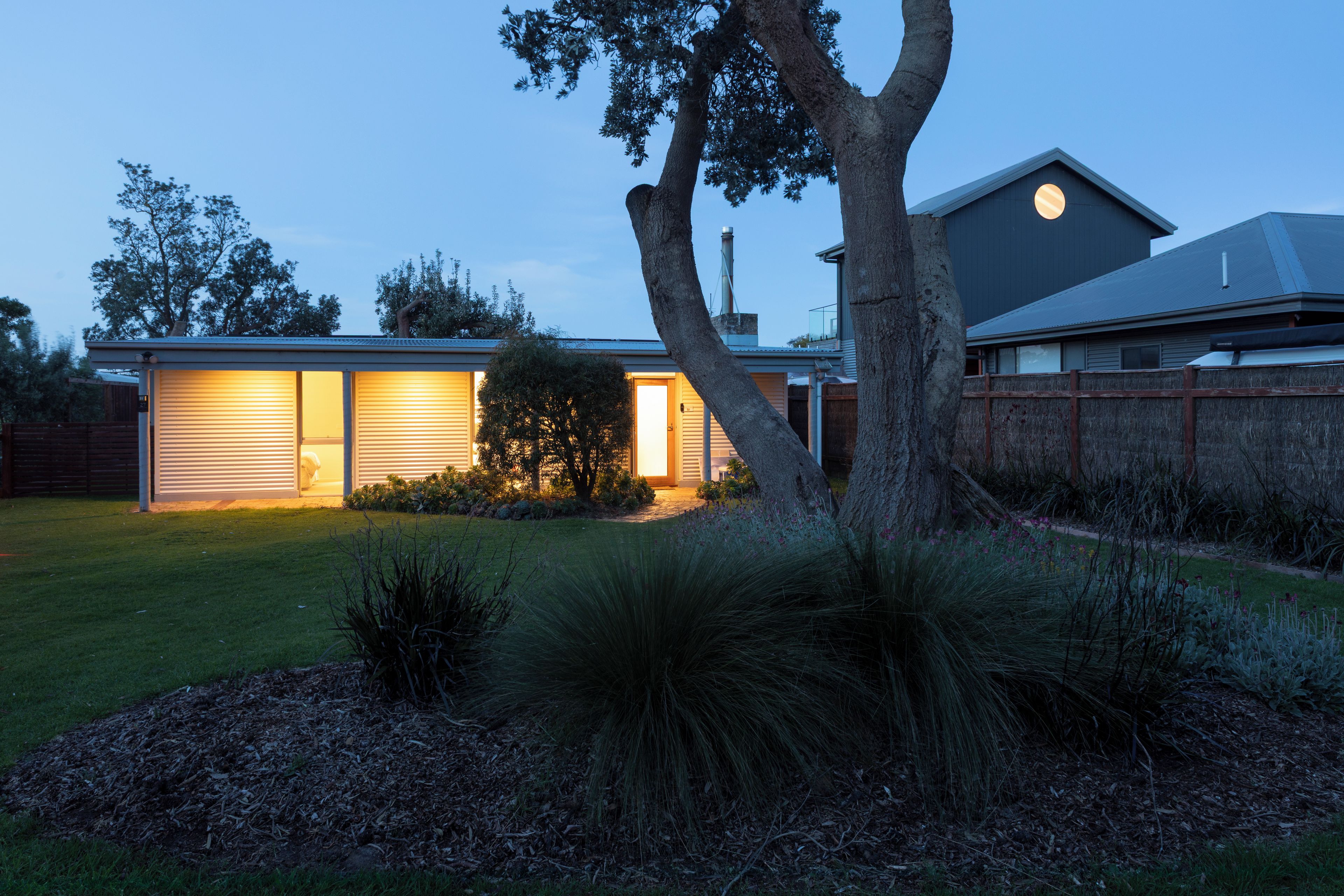 Une maison moderne avec un garage, un arbre dans le jardin et une clôture.