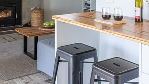 Een moderne keuken met een houten kookeiland, twee zwarte krukken, een wijnfles en glazen op het aanrecht.