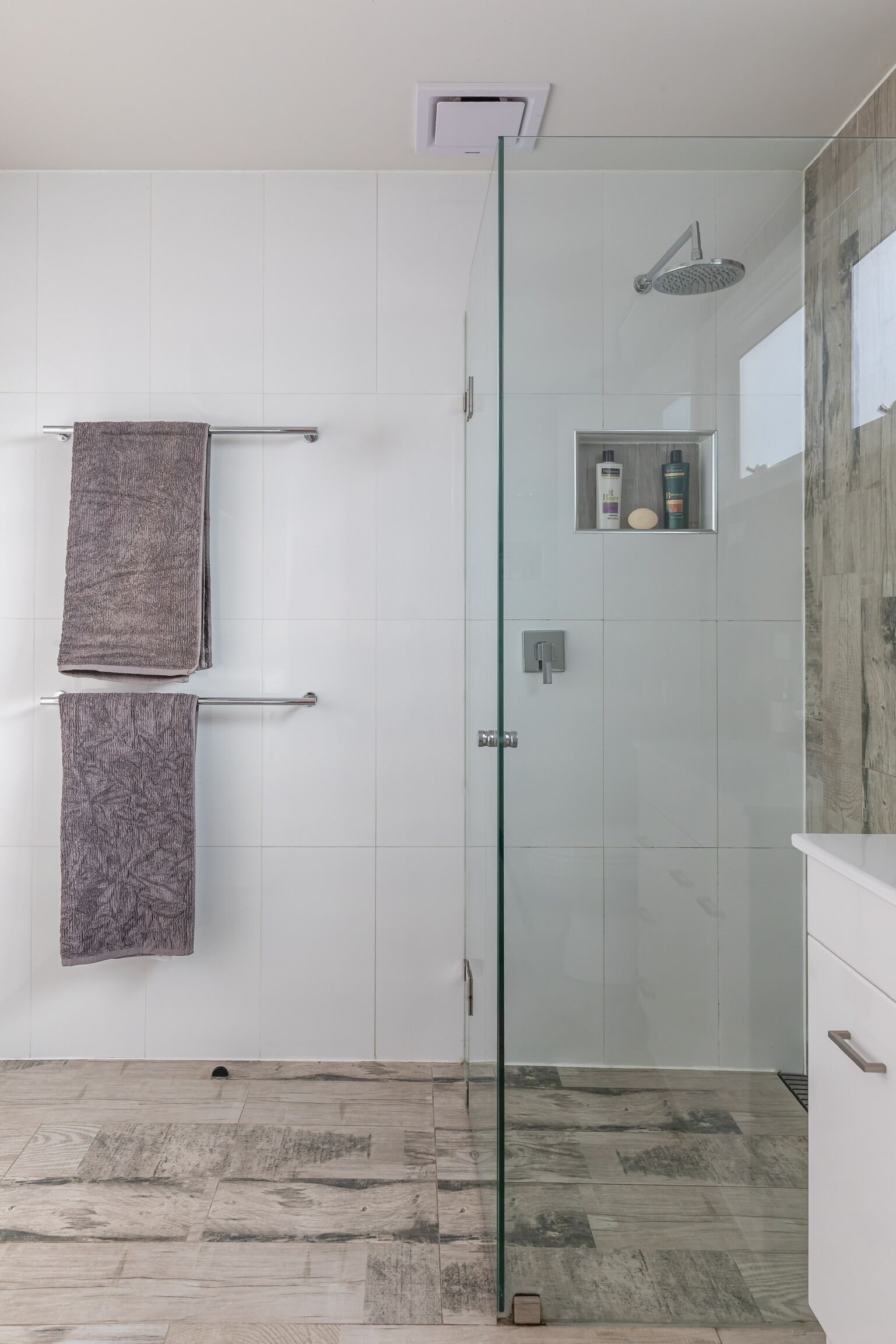 A modern bathroom with a glass-enclosed shower, white tiled walls, and a wooden floor.