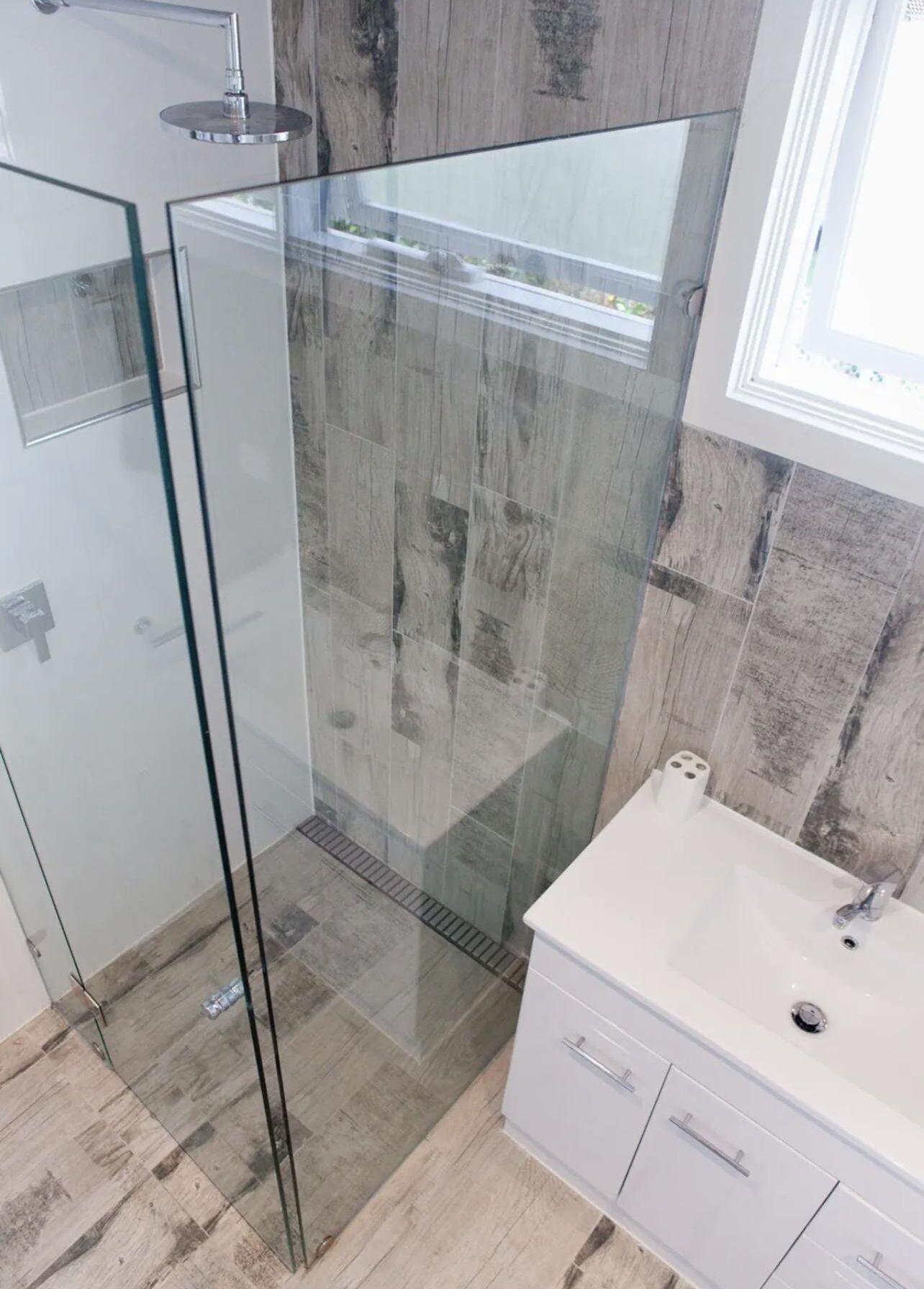 A modern bathroom with a glass shower enclosure, a white sink, and a wooden wall backsplash.