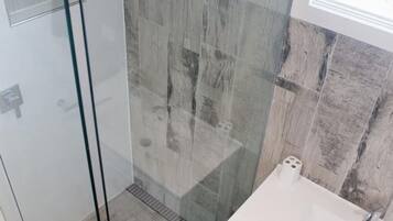 A modern bathroom with a glass shower enclosure, a white sink, and a wooden wall backsplash.