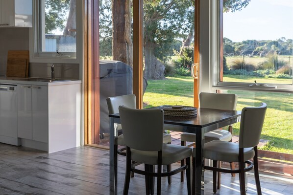 A modern kitchen with a dining area, large windows, and a view of the outdoors.