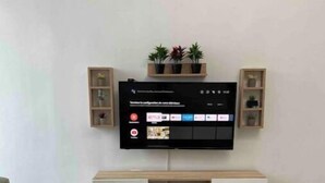 Een moderne woonkamer met een flatscreen televisie aan de muur, een houten salontafel en een minimalistische witte kast onder de televisie.