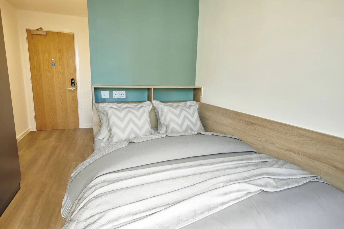 Um quarto com cabeceira de madeira, cama com roupa de cama cinza e uma parede em tom de verde-água.