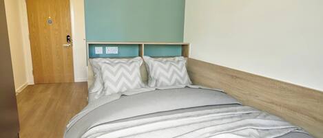A bedroom with a wooden headboard, a bed with grey bedding, and a teal accent wall.