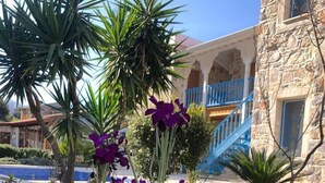 A garden with purple flowers and a stone building with a blue staircase. - La petra boutique hotel (Datça)