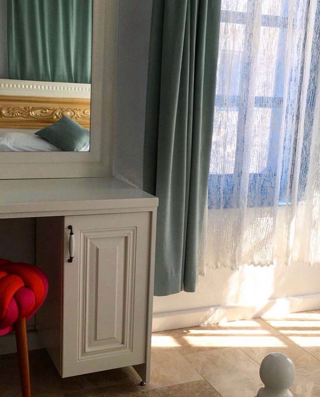 A room with a white vanity, a mirror, a green curtain, and a window with sunlight.