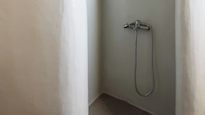 A small, enclosed shower area with a showerhead and hose, surrounded by plain walls. - Opulent Retreat Junior (Mykonos)