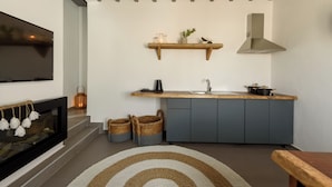 A modern kitchen with a wooden countertop, grey cabinets, a built-in stove, and a hanging shelf with decorative items. - Opulent Retreat Junior (Mykonos)
