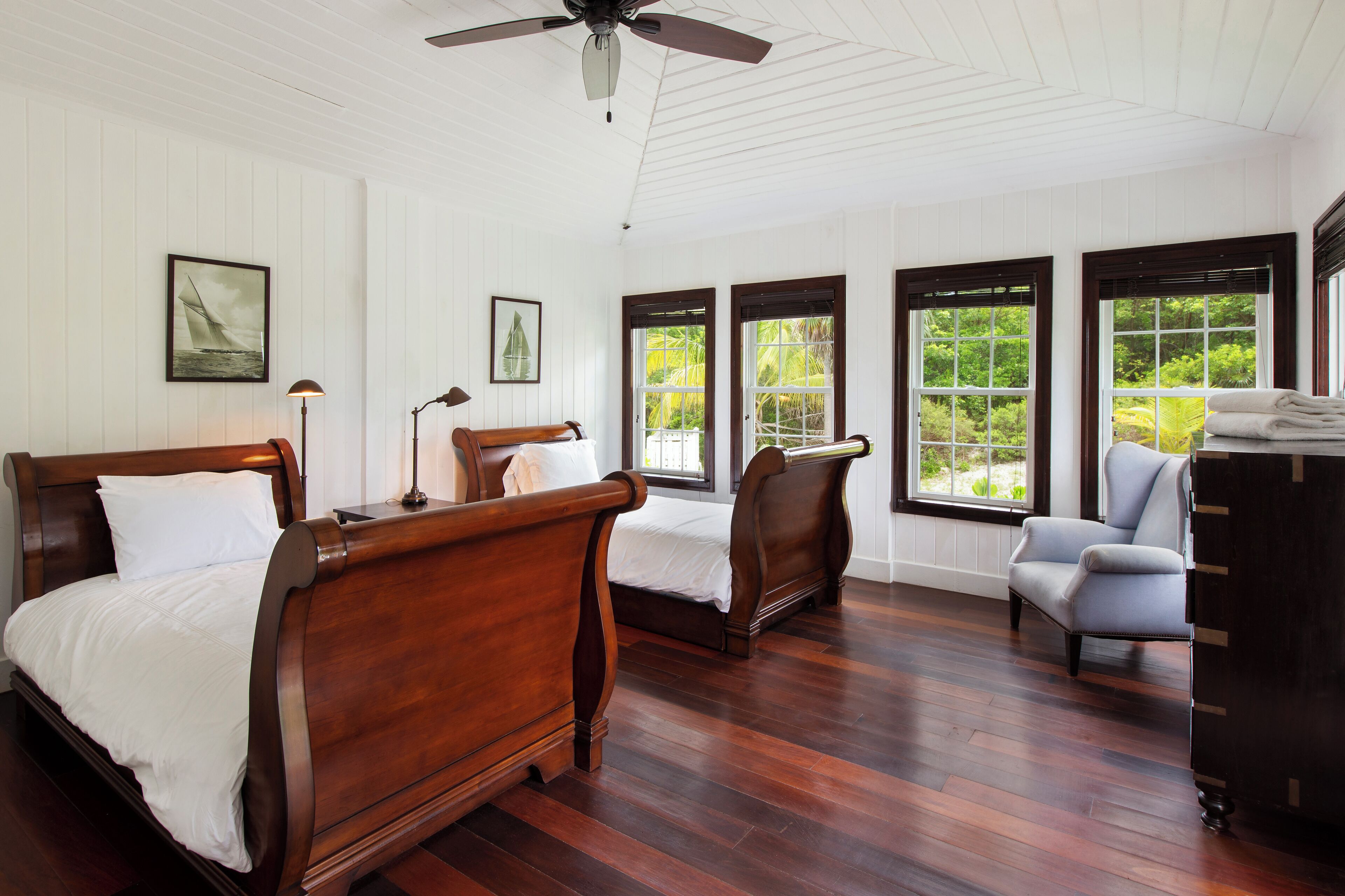 A bedroom with two wooden beds, a chair, and a dresser.