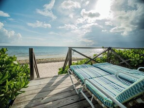 A beach view with a wooden deck and a lounge chair with striped cushions. - Flipper'S Haven: Tropical Retreat (North Palmetto Point)