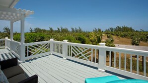 A wooden deck with white railings, outdoor furniture, and a view of a landscaped area with trees and a clear sky. - Caribbean Cliffside: Private Waterfront Retreat (North Palmetto Point)