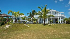A white colonial-style building with a covered porch and multiple balconies, surrounded by palm trees and a well-maintained lawn. - Caribbean Cliffside: Private Waterfront Retreat (North Palmetto Point)