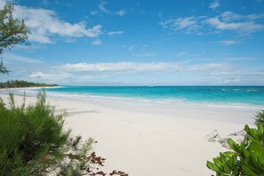 Een strand met wit zand en turquoise water, omringd door begroeiing en rotsen.