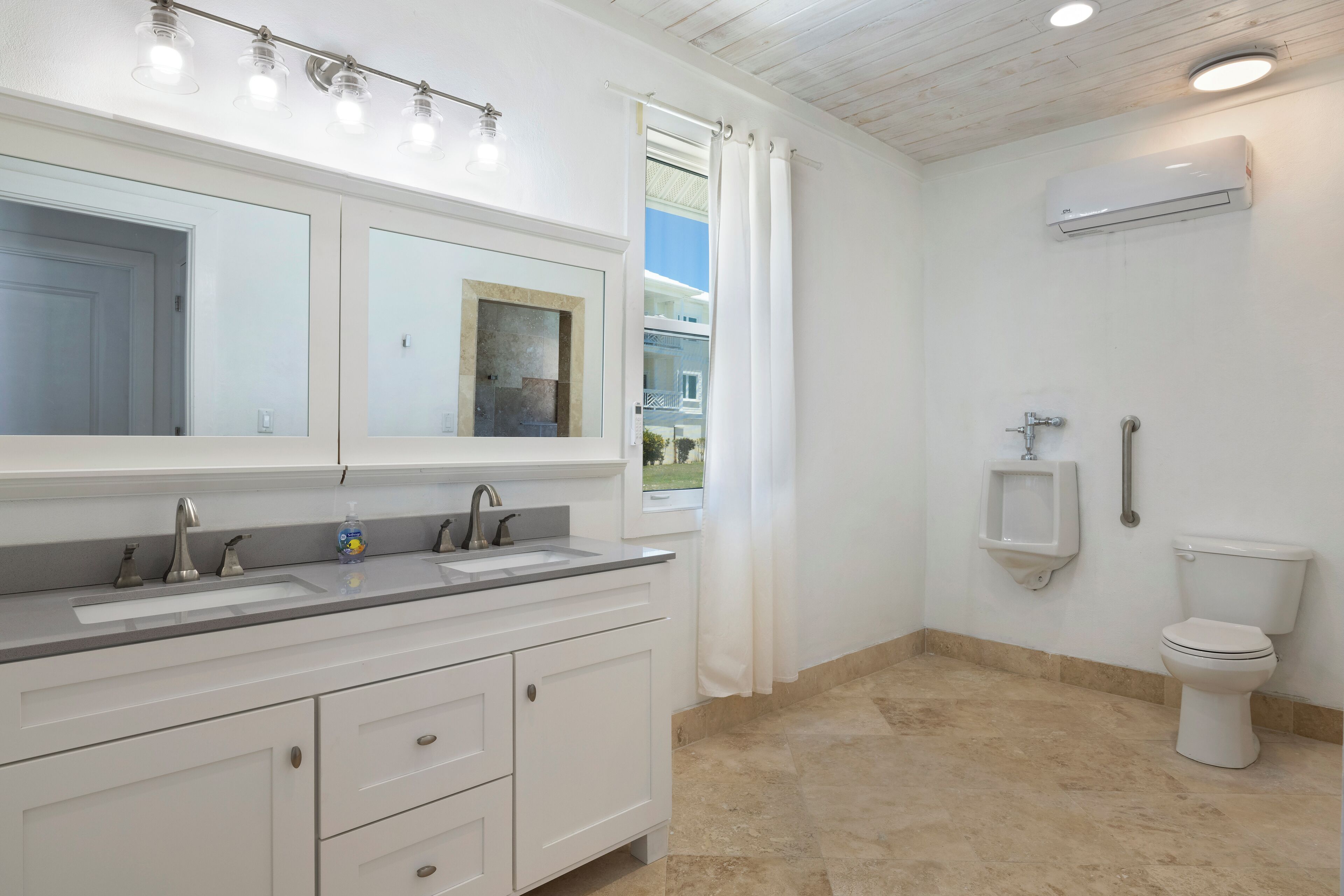 Une salle de bain équipée d’un meuble-lavabo à deux vasques, de toilettes et d’un urinoir.