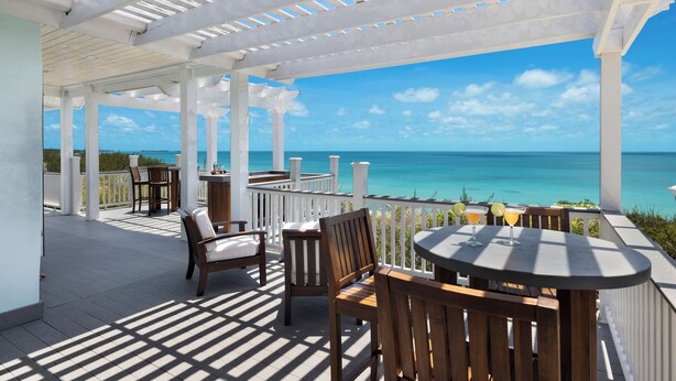 A covered outdoor area with wooden furniture and a view of the ocean. - Island Getaway: Charming Cottage Steps From The Beach (James Cistern)