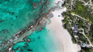 Vista aérea de un resort en la playa con aguas turquesas cristalinas, una playa arenosa y algunos edificios con piscina.