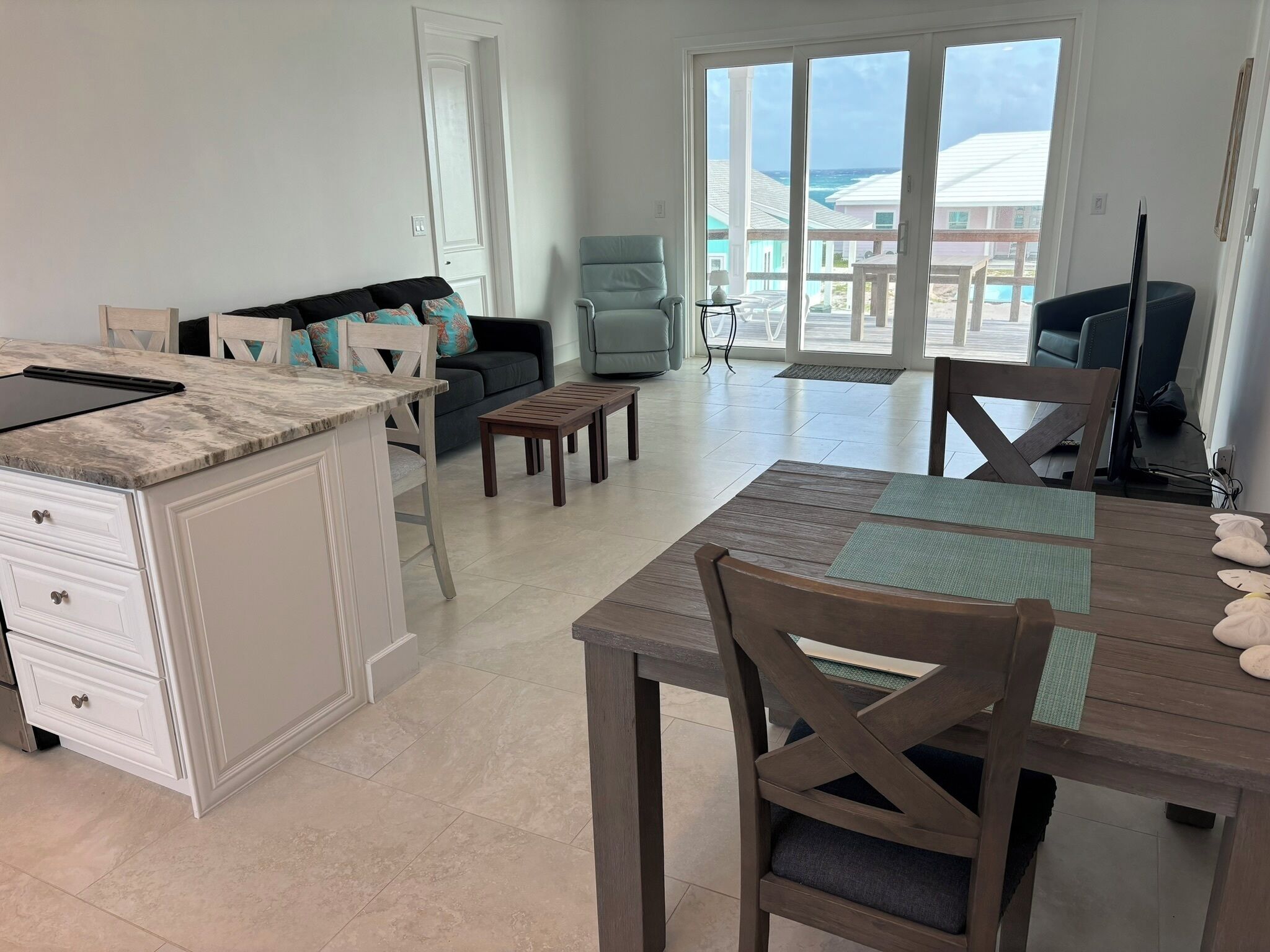 A spacious living area with a kitchen, a dining table with chairs, a sofa, and a view of the ocean through large windows.