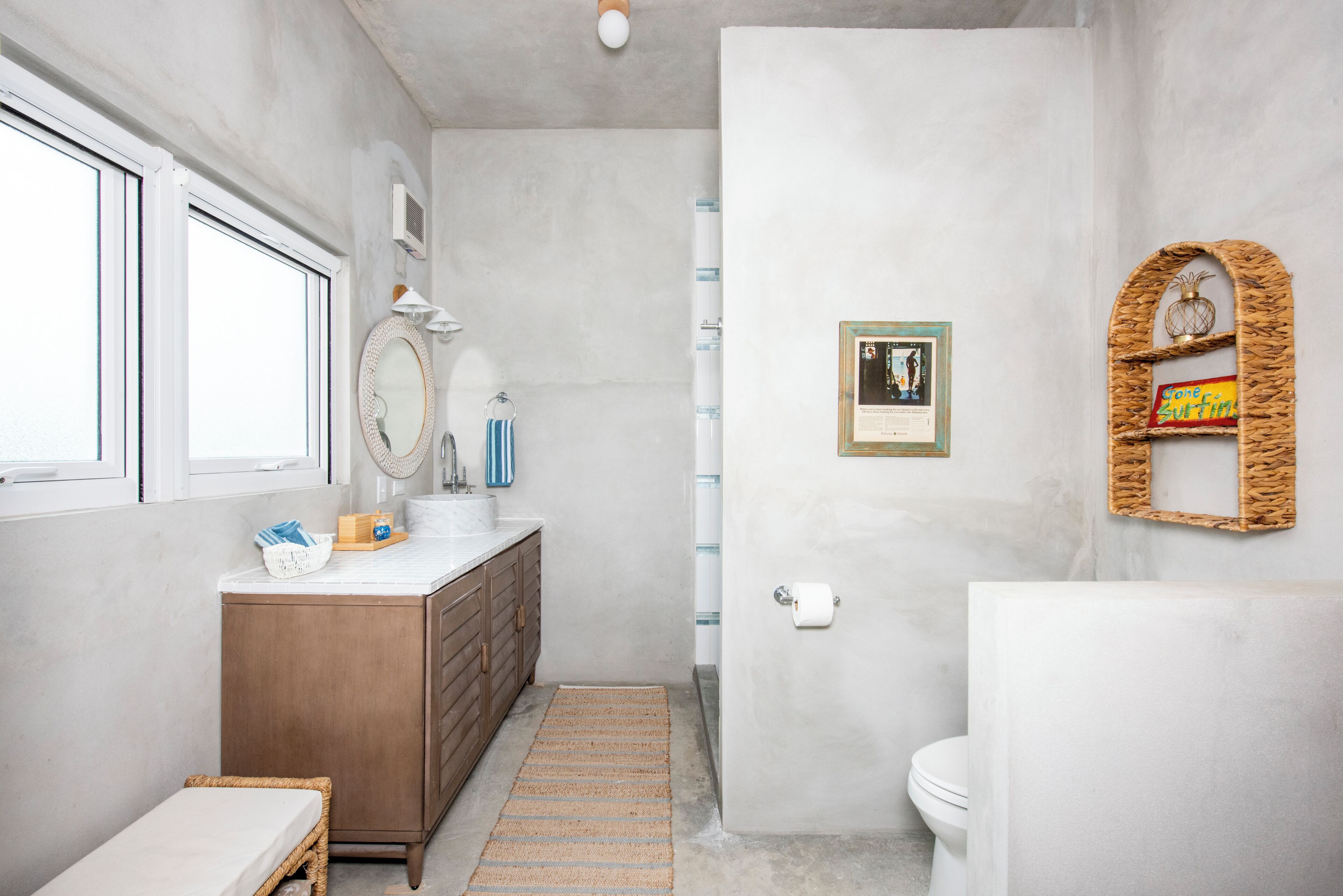 A bathroom with a marble sink, wooden vanity, a small wicker basket, a framed picture, and a toilet.