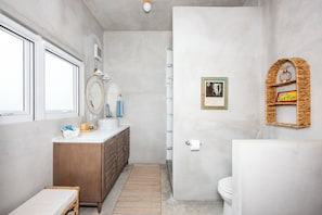 A bathroom with a marble sink, wooden vanity, a small wicker basket, a framed picture, and a toilet.