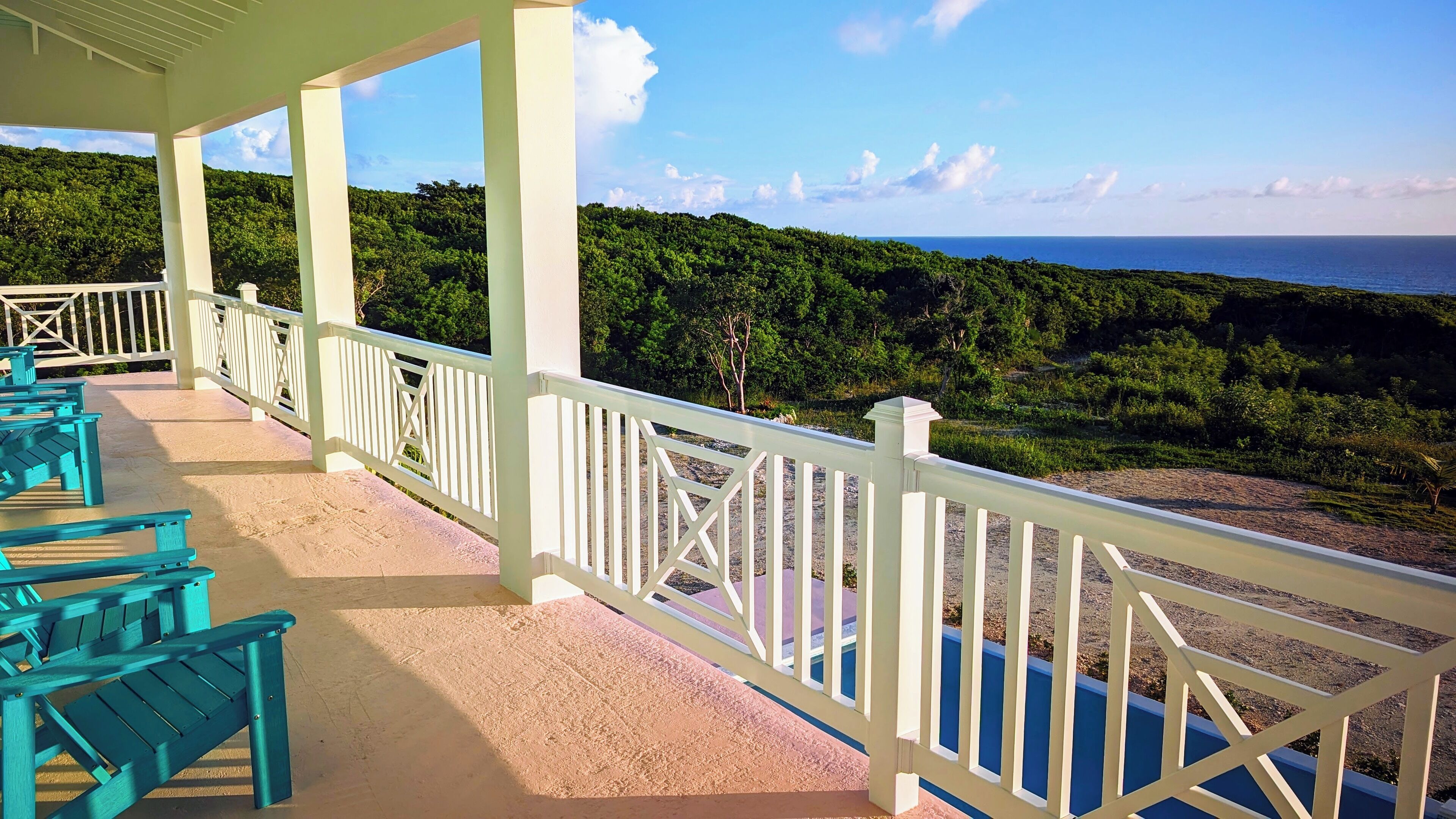 Un espace extérieur abrité, doté de rampes blanches et de bancs turquoise, qui offre une vue imprenable sur un paysage verdoyant et la mer.