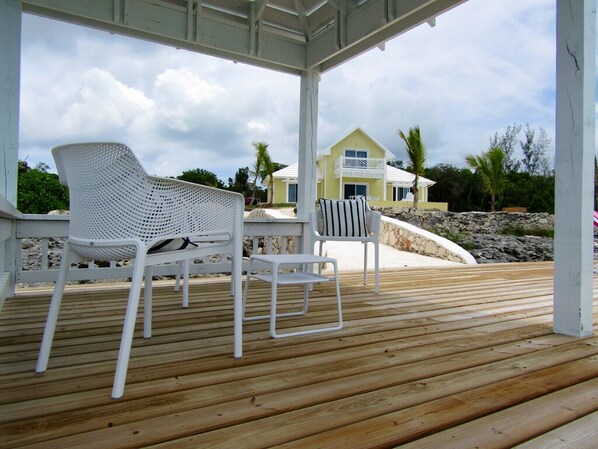 A wooden deck with white outdoor furniture, including a chair and a table. - Oceanfront Haven: Elegant Estate With Private Deck (James Cistern)