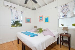 Une chambre à coucher avec un lit, une fenêtre avec des rideaux, un climatiseur fixé au mur et des tableaux encadrés.