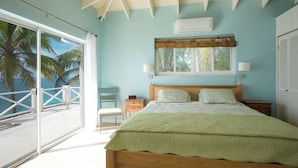 A bedroom with a large bed, a wooden headboard, a window with a view of palm trees, and an air conditioning unit.