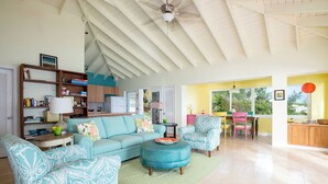 A spacious living room with a high ceiling, a dining area with a table and chairs, and a kitchen area with cabinets and a refrigerator.