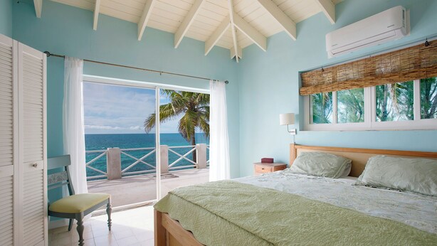 A bedroom with a bed, a nightstand, a chair, and a view of the ocean.